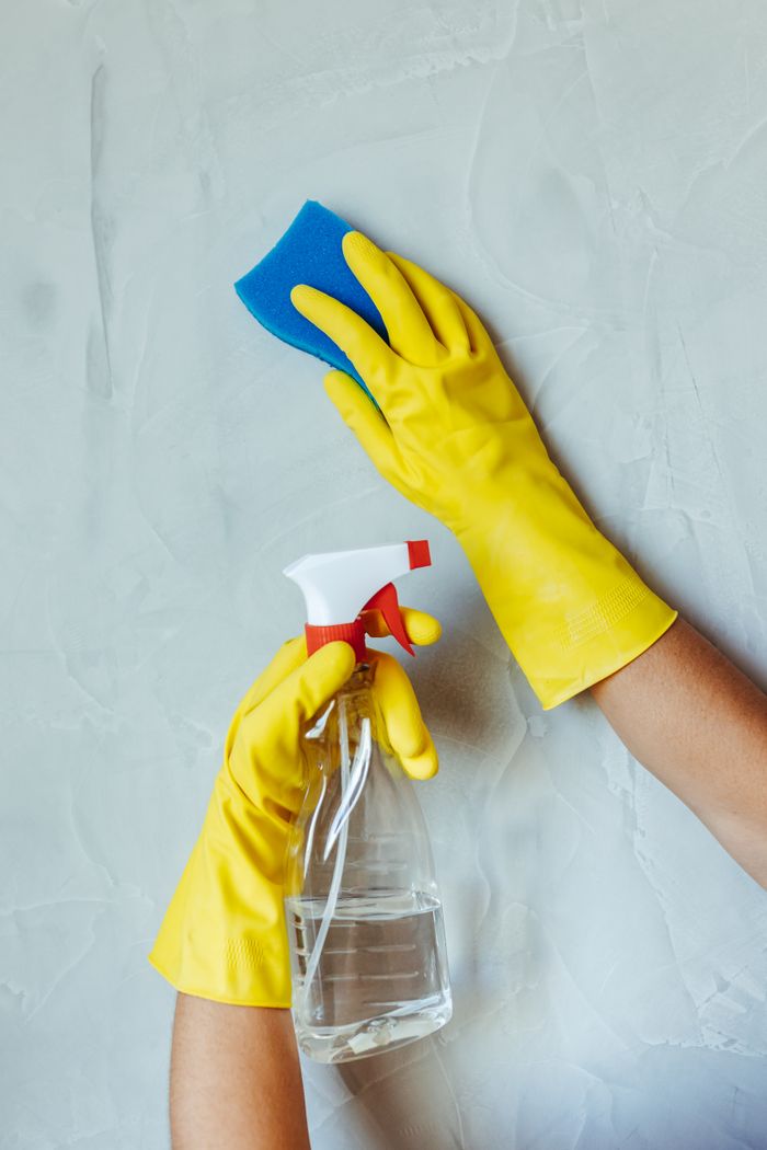 who-we-are Hands in yellow gloves cleaning wall with sponge and spray bottle.